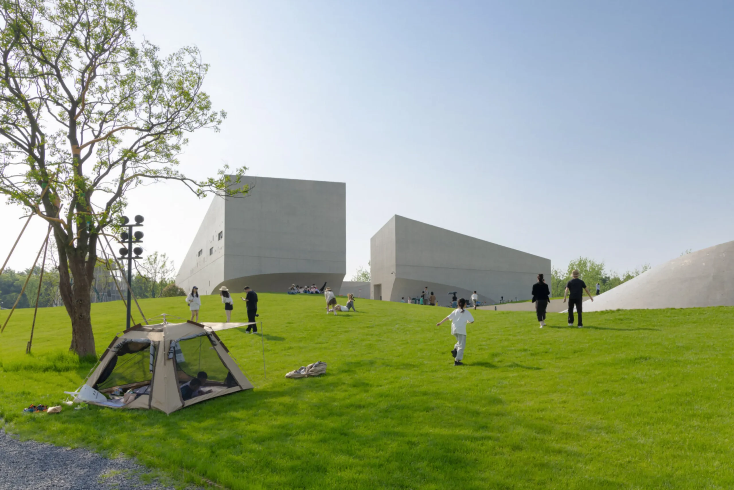 People relaxing, walking and picnicking on the grassy slopes in front of the pale concrete museum buildings under a clear blue sky