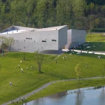 Aerial perspective of the pale concrete museum beside the lake, with visitors scattered across the green lawns and pathways